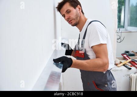 Male worker plastering a wall using a long spatula. Renovation concept Stock Photo
