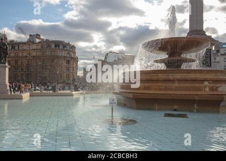 General view of one of the two fountains on Trafalgar Square London with a background of buildings and Nelson's Column. Stock Photo