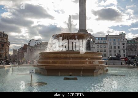 General view of one of the two fountains on Trafalgar Square London with a background of buildings and Nelson's Column. Stock Photo