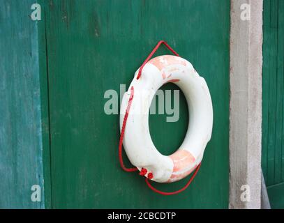 aged faded red and white plastic lifebuoy hanging on the wall of a vintage green door background Stock Photo