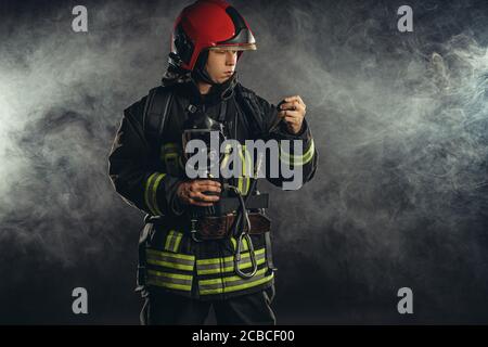 brave firefighter extinguishing fire in smoke, using special equipment and wearing uniform and helmet Stock Photo