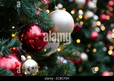 Red and silver christmas balls on a fir branches on festive golden lights background, street illumination. New Year tree with decorations Stock Photo