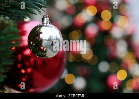 Red and silver christmas balls on a fir branches on festive golden lights background, street illumination. New Year tree with decorations Stock Photo