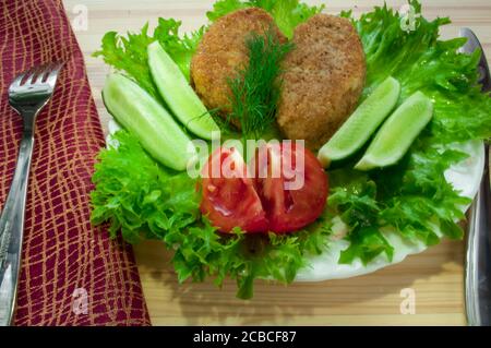 portion of potato cutlets on a plate with vegetables (cucumber, tomato) and greens (lettuce, dill) Stock Photo