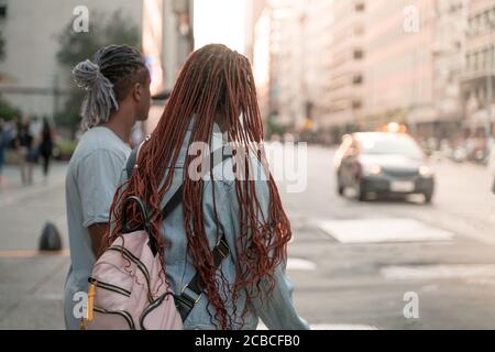 A black couple standing at a road in the city waiting to cross.