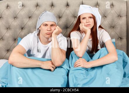 We should go to bed earlier. Sleepy tired couple sitting in bed canot wake up in morning. close up photo. bad morning Stock Photo