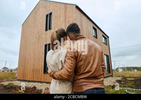 Couple stand, hug and look at big new house Stock Photo