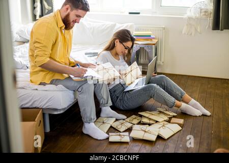 happy caucasian married couple sorting letters at home, they going to invite guests in their new house, housewarming. they make notes on laptop and pr