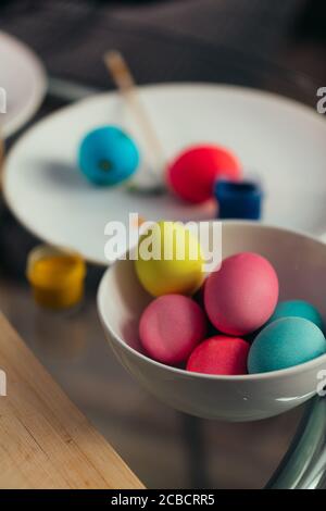 Easter eggs with pastel colors a sitting in a plain white ceramic bowl with cans of paints on background Stock Photo