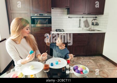 Blonde Female babysitter having confidence, skill and understanding to support children's play, interacting with boy in a playful way, painting eggs t