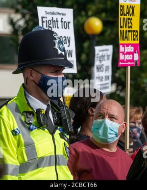 Police officer wearing blue face mask, at an NHS hospital workers protest demonstration in central London, with curious protester looking up at him. Stock Photo