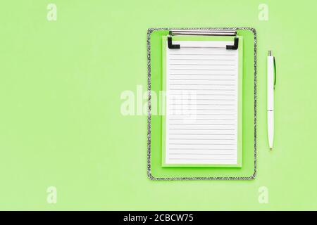 Blank clipboard mockup and white ballpoint pen on green color background. Top view, copy space for text. Back to school, deadline, morning concept.