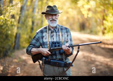 Portrait of positive hunter man holding gun, stand in forest Stock Photo