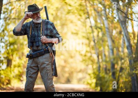 Bearded caucasian man in hunting clothes stand looking away. Forest background