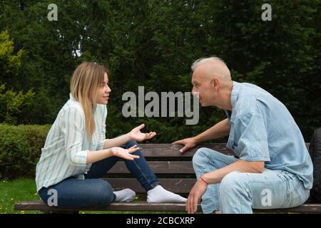 man with gray hair and caucasian woman are sitting on a bench and talking Stock Photo