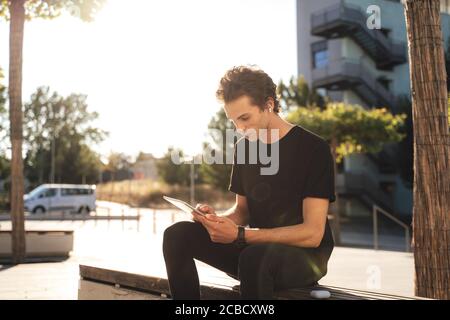 Handsome European businessman working on tablet computer while sitting on bench in city Stock Photo