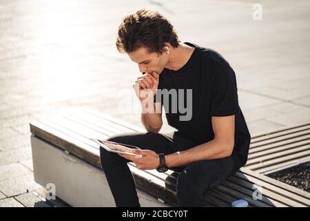 Young university student studying online on tablet computer while sitting on bench at campus Stock Photo