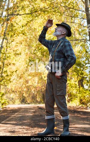 Bearded caucasian hunter wearing cowboy hat in search of trophy in autumn forest, look uo for wild bird. Stand looking for prey in hunting period, aut Stock Photo