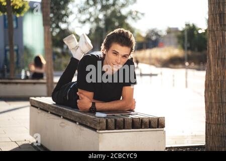 Full length portrait of handsome Caucasian man lying on bench at university campus on sunny day Stock Photo