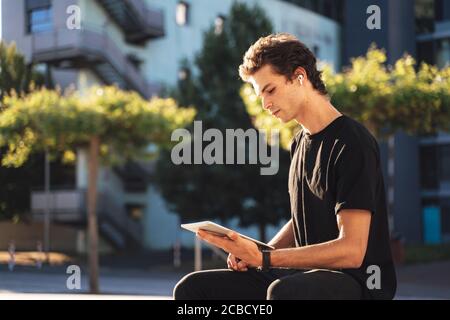 Handsome young man studying online on digital tablet while sitting at college campus Stock Photo