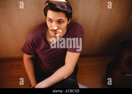 Thoughtful young man sitting on balcony floor at home Stock Photo