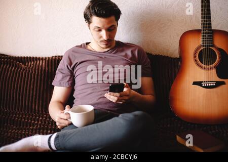 Surprised young man using smart phone while drinking tea at home Stock Photo