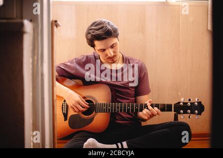Young man playing guitar while sitting on balcony floor at home Stock Photo