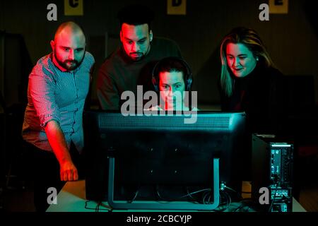 A woman gathers a team of students around computer in dark room Stock Photo