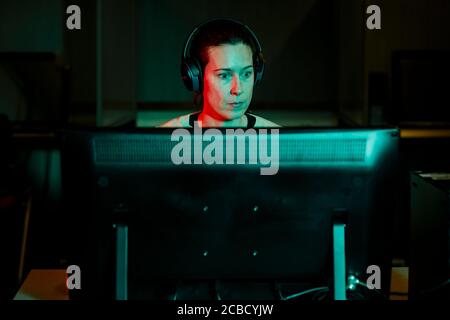 Front view of a woman in headphones working at computer in dark room Stock Photo