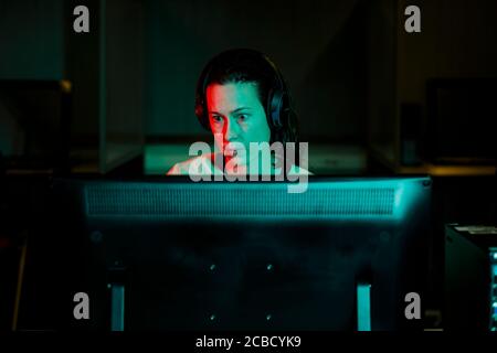 A woman with an intense gaze works at desktop computer in dark room Stock Photo