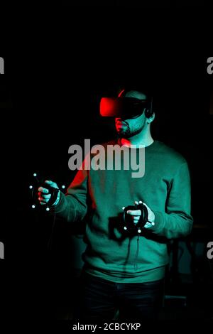 A young man wearing virtual reality glasses stands in a darkened room Stock Photo