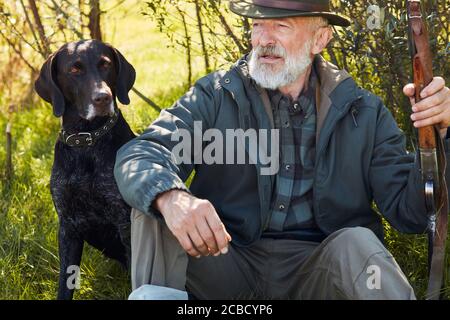 Mature bearded man after hunting in autumn forest, sit having rest Stock Photo