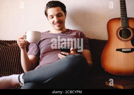 Happy young man using smart phone while drinking tea at home Stock Photo