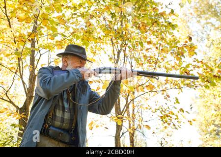 Concentrated hunter holding rifle and waiting for prey, hunter shooting in autumn forest. Hunting season Stock Photo