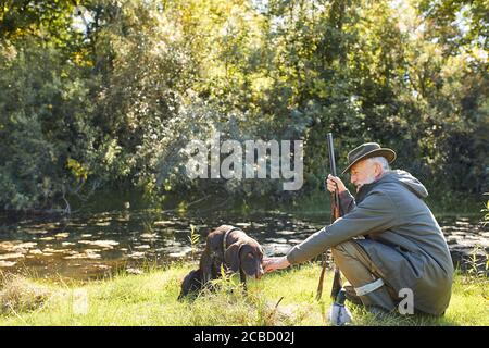 Have rest before hunting. Hunter man on lake, holding rifle Stock Photo