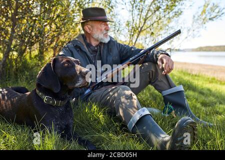 Looking for trophy with dog. Senior man ready to hunt. Sit having rest before hunting Stock Photo