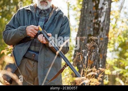 Cropped hunter load rifle and going to shoot.Male in hunting casual clothes, autumn forest background Stock Photo