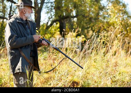 Senior man look away in search of trophy loading rifle going to shoot on wild animals. Hunting as hobby Stock Photo