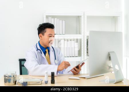 Asian man doctor wears white coat and headset speaking videoconferencing on laptop computer using online video call consultation app. Remote medical h Stock Photo