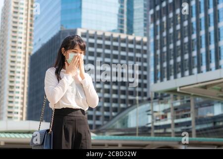 Young Asian businesswoman in white shirt going to work feeling sick with cough wears protection mask prevent PM2.5 dust, smog, air pollution and COVID Stock Photo
