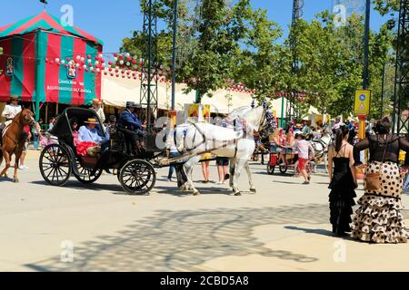 Horse drawn carriage and riders in traditional Spanish garb during the 2019 Corpus Christi Fair celebration in Granada, Spain; Sevillanas, flamenco. Stock Photo