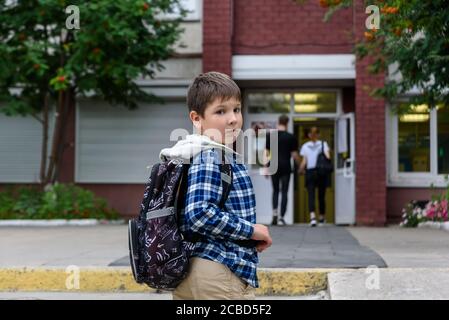 Child boy with bag stays near elementary school and looks to the camera Stock Photo