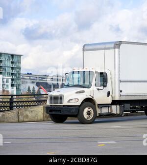 Middle size compact powerful rig semi truck with box cargo trailer for local deliveries driving on the bridge on the city street Stock Photo