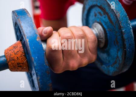 Young man lifting old blue gym weights on the floor in a gym Stock Photo