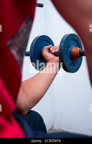 Young man lifting old blue gym weights on the floor in a gym Stock Photo
