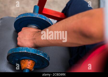 Young man lifting old blue gym weights on the floor in a gym Stock Photo
