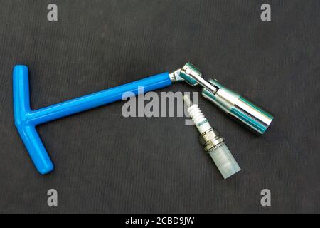 blue hinged key for spark plugs of an internal combustion engine needed at the service station and new sparking plug on a black surface Stock Photo