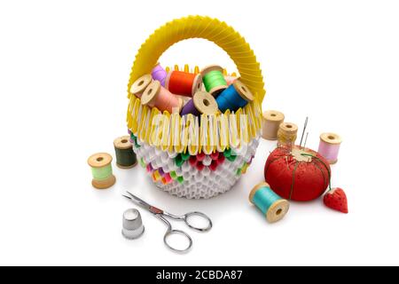 Colorful origami basket with spools of thread, pin cushion, scissors, and thimble on a white background. Stock Photo