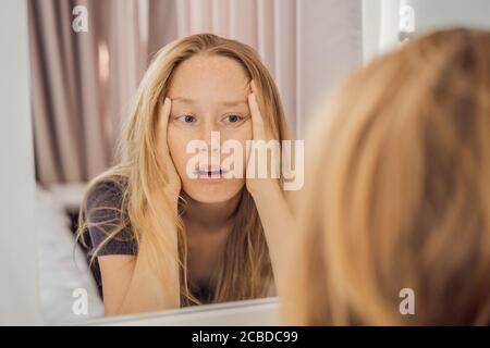 Extremly tired young woman looking at himself in the mirror, home alone. self-isolation at home, quarantine due to pandemic COVID 19. Mental health Stock Photo