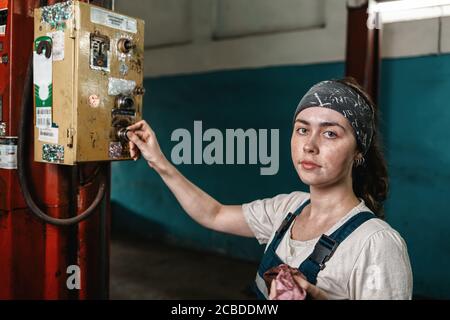 The concept of small business, feminism and women's equality. A young woman presses a button on the factory working mechanism and poses. Stock Photo